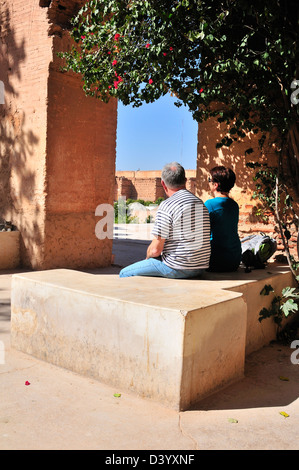 I turisti, maschio e femmina, vista posteriore del piano di appoggio e di seduta al di sotto di albero in motivi di El Badii Palace, Marrakech, Marocco Foto Stock