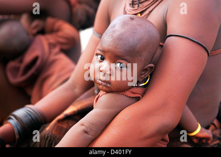 Bambino nella madre di braccia di Himba tribe con pelle rossa coperto di otjize, una miscela di grasso di burro e ocra, Namibia, Sud Africa Foto Stock