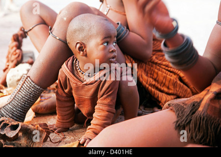 Baby e le donne della tribù Himba con pelle rossa coperto di otjize, una miscela di grasso di burro e ocra, Namibia, Sud Africa Foto Stock