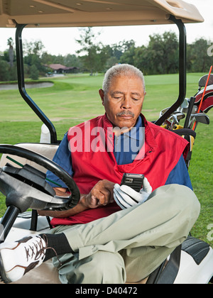 Uomo nero utilizzando il cellulare in golf cart Foto Stock