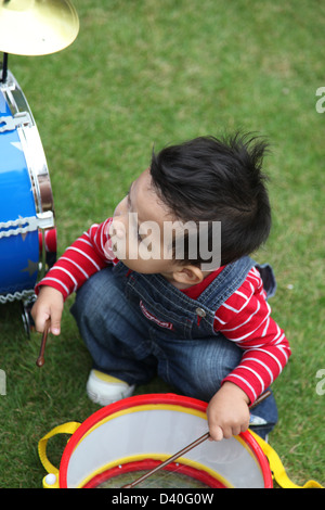 Si tratta di una foto di un giovane bambino ragazzo che sta suonando la batteria su un ragazzo giocattolo strumento musicale tamburi. È di colore blu e sull'erba Foto Stock