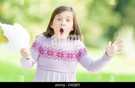 Ritratto di graziosa bambina in abito lilla con cotone candy in mano all'aperto. Bambino Piccolo nel parco guardando sorpreso e shock Foto Stock