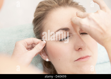 Giovane donna avente le sopraciglia filettato, per rimuovere i peli indesiderati. Questa tecnica consente un controllo estremamente preciso relativamente liberi dal dolore Foto Stock