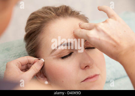 Giovane donna avente le sopraciglia filettato, per rimuovere i peli indesiderati. Questa tecnica consente un controllo estremamente preciso relativamente liberi dal dolore Foto Stock