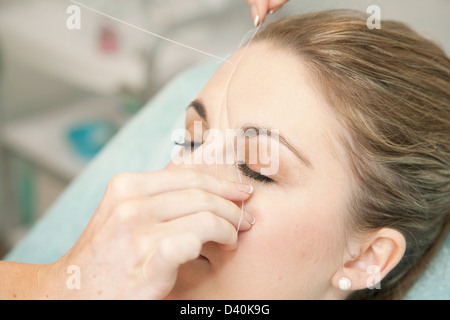 Giovane donna avente le sopraciglia filettato, per rimuovere i peli indesiderati. Questa tecnica consente un controllo estremamente preciso relativamente liberi dal dolore Foto Stock