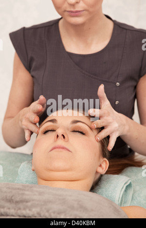 Una giovane donna con i punti di pressione sul suo tempio massaggiato. Foto Stock