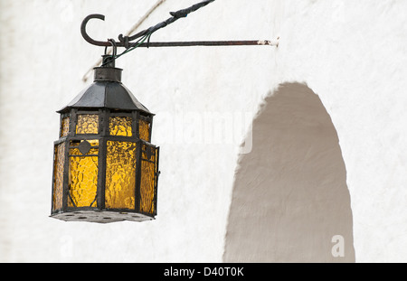 Nero lanterna vintage con giallo vetro di sfiato appesa al gancio sopra arcuata di entrata o la finestra nel vecchio muro bianco. Esterno e faca Foto Stock