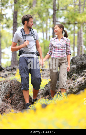 Sorridenti interracial giovane holding hands godendo romantica passeggiata nella foresta di primavera con fiori Foto Stock