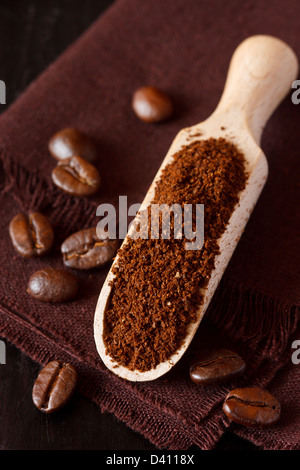 Caffè macinato fresco in una paletta di legno e i chicchi di caffè su uno sfondo di colore marrone. Foto Stock