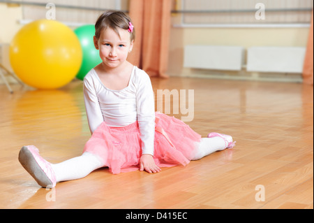 Carino piccolo balerina stretching sul pavimento in palestra Foto Stock