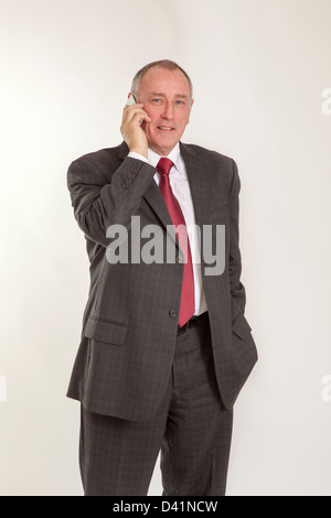 Uomo maturo in 50s che indossa un abito grigio, parlare su un telefono cellulare o un telefono cellulare, cercando di fotocamera a sorridere. Foto Stock