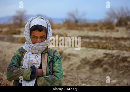 A Kandahar, Afghanistan - 10 Gennaio 2011: un ragazzo afgano sfugge il freddo gennaio meteo in un vecchio campo foderato giacca. Foto Stock