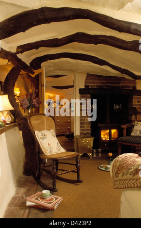 La canna da zucchero-indietro Sedia a dondolo in piccoli cottage soggiorno con stufa a legna e bassa, travi a soffitto Foto Stock