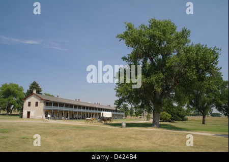 Blue sky view alberi sollevandosi al di sopra di white prairie schooner di carro e lunga caserma di cavalleria edificio, Fort Laramie, Wyoming USA Foto Stock