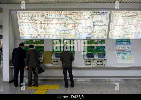 Imprenditori e un " commuter " acquistare i biglietti del treno da distributori automatici di seguito illuminato mappe ferroviarie all'interno della stazione di Tokyo. Foto Stock