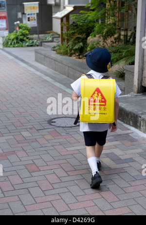 Scuola elementare ragazzo con tappo a casa a piedi da scuola a Tokyo. Di colore giallo brillante zaino indica 'kotsu anzen' La sicurezza del traffico. Foto Stock