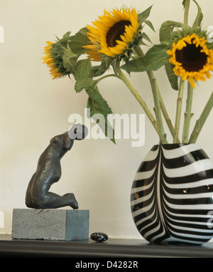 Close-up della figurina inginocchiato accanto al giallo dei girasoli in bianco e nero a strisce vaso Foto Stock