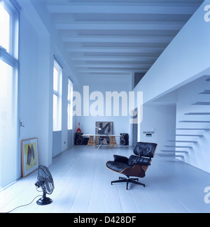 Il nero Charles Eames no.671 lounge chair e ventola elettrica in conversione loft hall dipinta con pavimento in legno e travi a soffitto Foto Stock