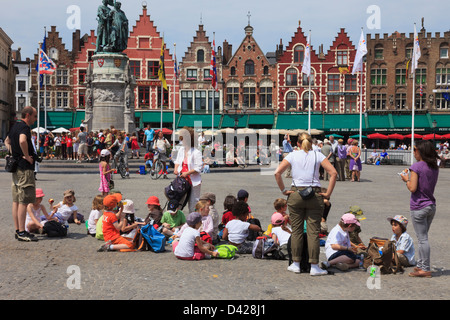 Markt, Bruges, Fiandre Orientali, Belgio. Gruppo di bambini in gita scolastica in seduta il quadrato di mangiare pranzo al sacco Foto Stock