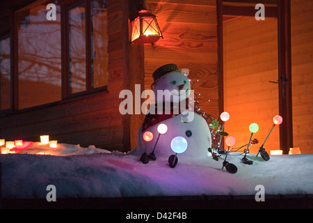 Francia, Ariège, pupazzo di neve di notte circondato con il solare luci da giardino, di fronte a una casa in legno Foto Stock