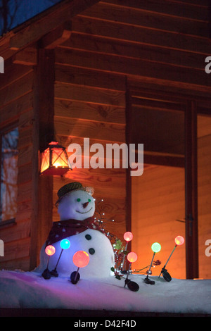 Francia, Ariège, pupazzo di neve di notte circondato con il solare luci da giardino, di fronte a una casa in legno Foto Stock