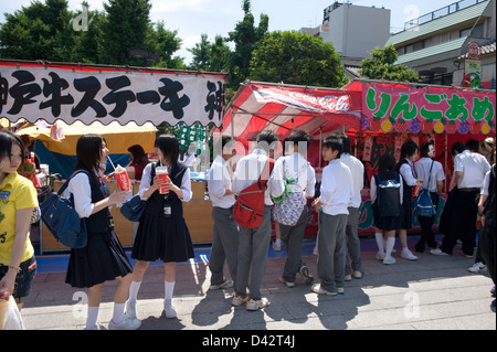 Alta scuola i ragazzi e le ragazze in uniforme godere di atmosfera festosa mentre passeggiando roten stand con giochi e spuntini Foto Stock