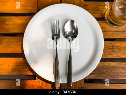 Cucchiaio e forchetta sul piatto bianco sul tavolo di legno Foto Stock