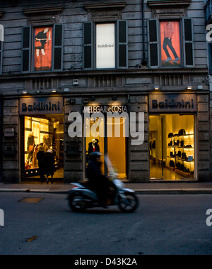 Ciclomotore passando Baldinini designer boutique store al crepuscolo e Via Montenapoleone Milano Lombardia Italia Europa Foto Stock