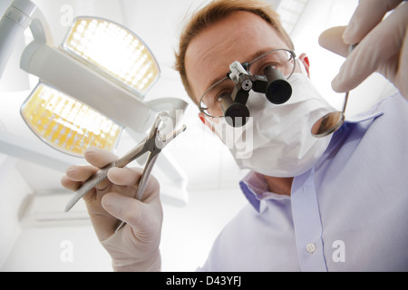 Dentista indossando maschera chirurgica con lente di ingrandimento guardando giù, Germania Foto Stock