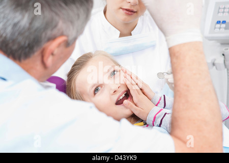 Ragazza di toccare la guancia con dentista e igienista dentale in ufficio, Germania Foto Stock