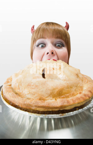 Giovane donna indossa diavolo corna e mangiare una torta Foto Stock