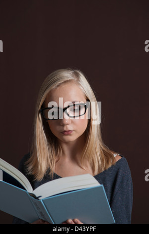 Ritratto di bionda, Teenage Grill indossando occhiali e la lettura di libro, Studio shot su sfondo nero Foto Stock