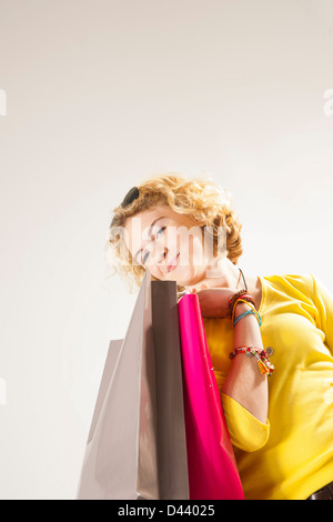 Ritratto di bionda, la ragazza con i capelli ricci, tenendo le borse della spesa e sorridente alla fotocamera, Studio shot su sfondo bianco Foto Stock
