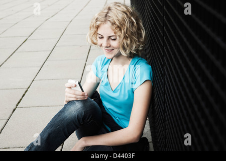 Ritratto di adolescenti Grill sorridente, seduto sul marciapiede tramite cellulare, Mannheim, Germania Foto Stock