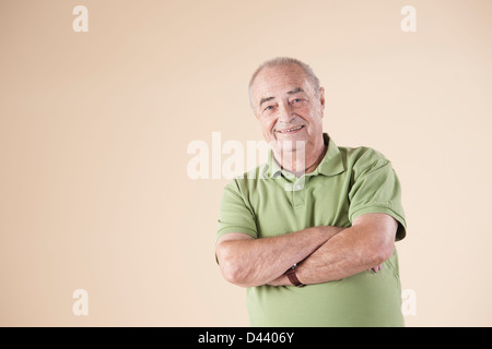 Ritratto di uomo anziano con le braccia incrociate, guardando la telecamera sorridendo, Studio shot su sfondo beige Foto Stock