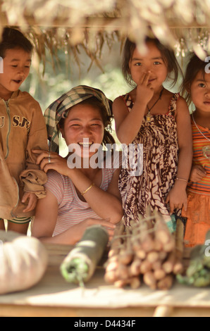 Tre bambini e una giovane donna vendita di ortaggi da una banchina in Laos Foto Stock