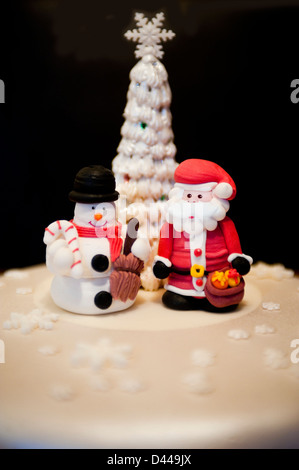 Verticale di chiusura del divertimento modellato figure di Babbo Natale e un pupazzo di neve in piedi su una torta di Natale. Foto Stock