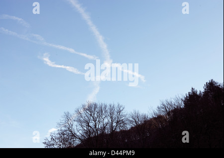 I percorsi del vapore dell'aeromobile formano un modello simile ad un uccello sopra il bosco, Galles, Regno Unito Foto Stock
