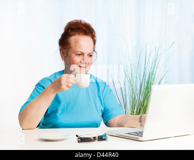 Bella Signora senior di bere il suo caffè del mattino e la lettura internet news Foto Stock
