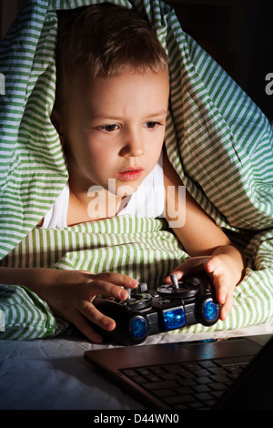 Poco cinque anni vecchio ragazzo giochi sul computer con console di gioco Foto Stock