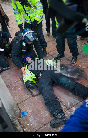 Poliziotto in piena riot gear trattando un inconscio collega, su un ampio Santuario off Piazza del Parlamento, giorno X3 manifestazione studentesca, Londra, Inghilterra Foto Stock