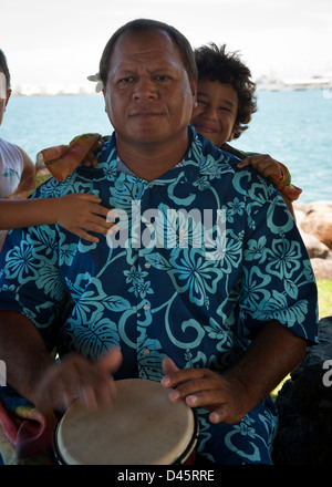Uomo polinesiano nella camicia floreale con bambini, giocando a percussione bongo, Papeete Foto Stock