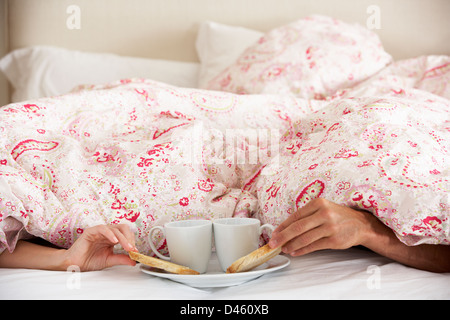 Coppia di mani di raggiungere da sotto il piumone per la prima colazione Foto Stock