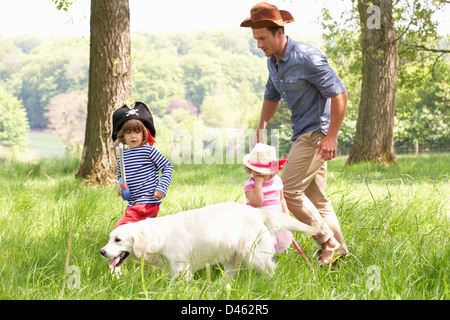 Padre giocando eccitante gioco di avventura con i bambini e il cane nel campo estivo Foto Stock