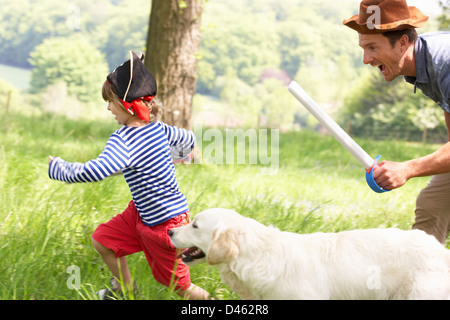 Padre giocando eccitante gioco di avventura con figlio e cane nel campo estivo Foto Stock