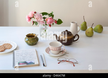 Ora del tè e biscotti con assortimento di stoviglie, un vaso di fiori e studio portatile su un tavolo Foto Stock