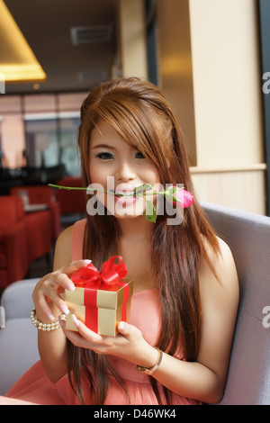 Giovane bella donna seduta su un divano mentre l'apertura di una confezione regalo. Foto Stock