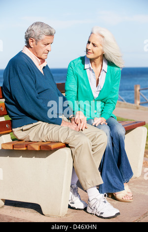 Senior donna consolante premuto marito seduta sul banco di lavoro Foto Stock