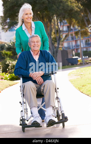 Senior donna spingendo il marito in carrozzella Foto Stock