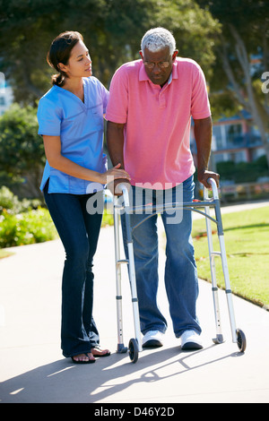 Accompagnatore aiutando Senior Uomo con telaio a piedi Foto Stock